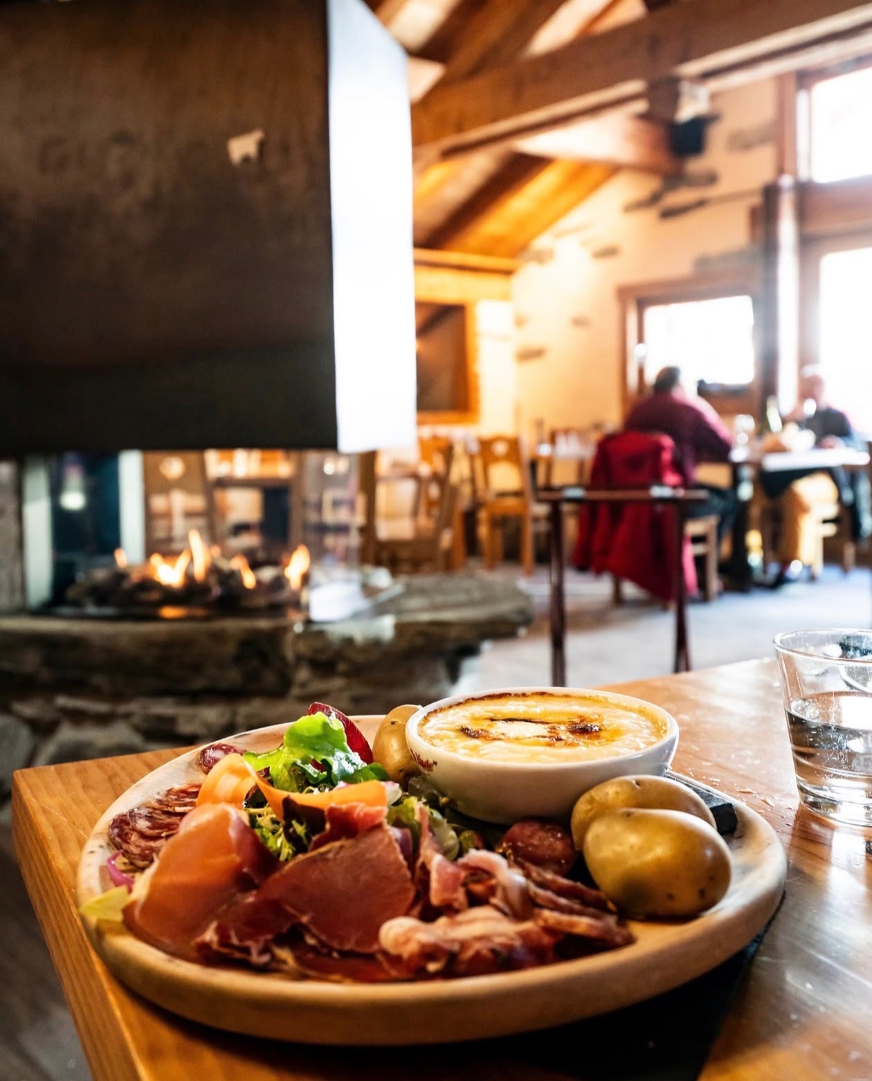 Fromage fondu gratiné, pommes de terre et charcuterie servis devant la cheminée du chalet